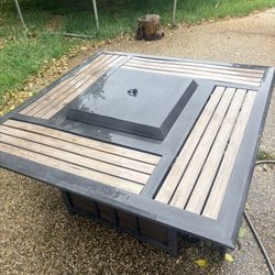 Cool outdoor fire pit table. Has wood slats and a dark frame. Uses propane gas. Includes a cover so you can use it as a regular table when not lit. St