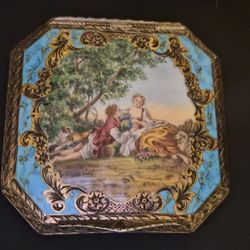 Elegant vintage powder compact by Germaine Monteil, featuring a beautifully detailed romantic courting scene framed in vibrant enamel and ornate gold