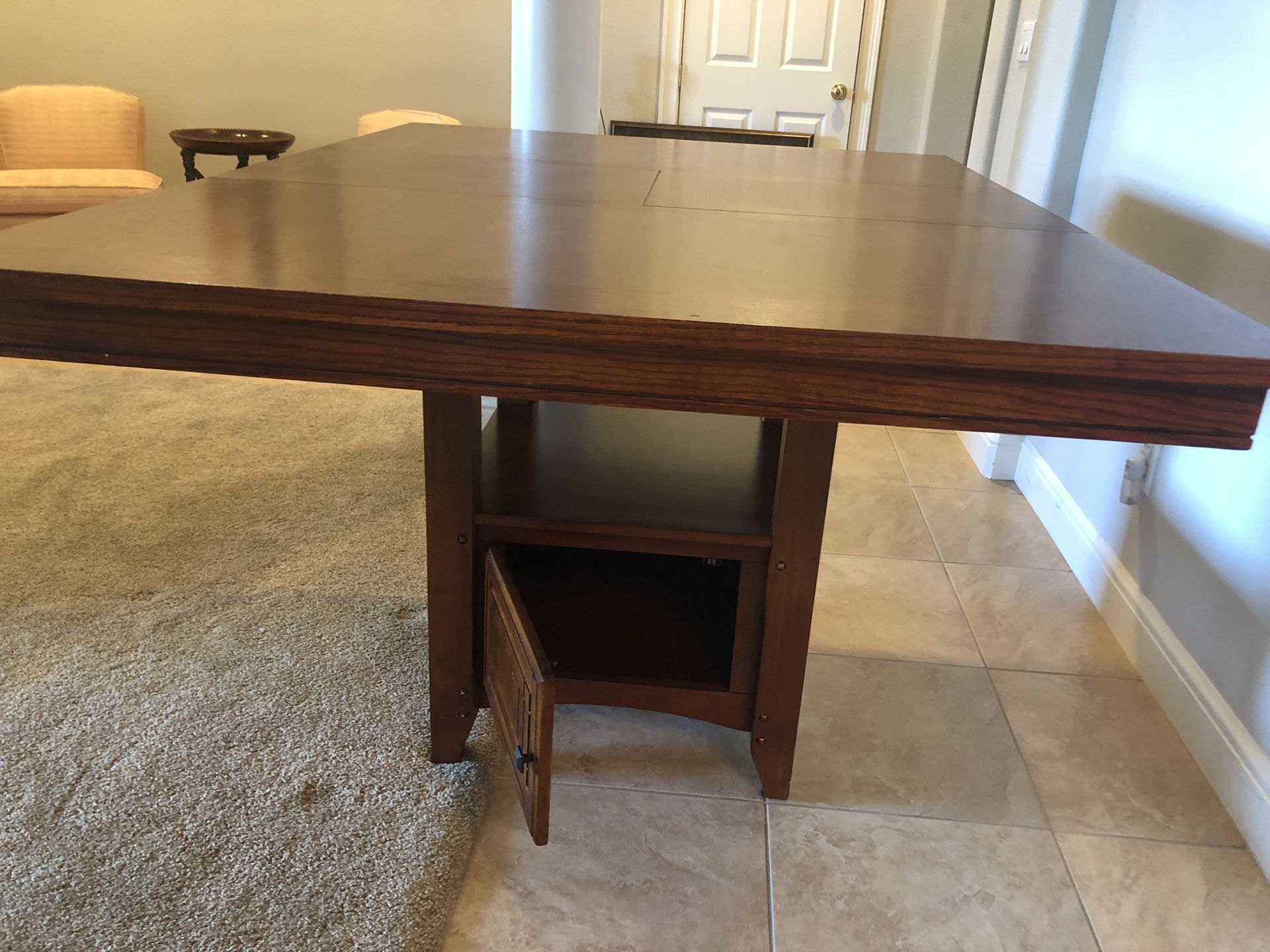 Bar height wood dining table. Can be square 48”x48” or rectangle with a middle leaflet. It has a storage and shelf under and is used but as good as n