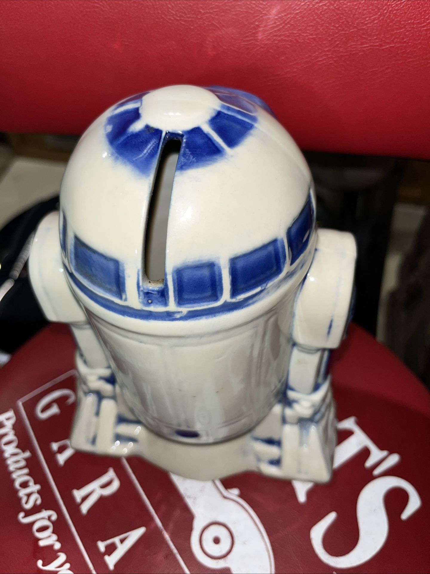 The image shows the bottom of a vintage R2-D2 ceramic coin bank. The text molded into the ceramic indicates it is a piece of official merchandise fro