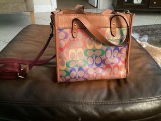 This Coach Field Tote 22 in Rainbow Signature Canvas features a vibrant rainbow-colored logo pattern and tan leather trim