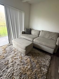 Cozy, deep-seated 93” sofa with a matching ottoman, Tan cement  w/ a pile shag area rug, multi-tone cream, beige, and grey abstract pattern.