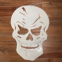 This Halloween decoration is a white plastic skull hanging ornament featuring cutout details of cracks and scars.
