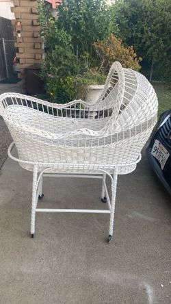 This vintage white wicker bassinet features wheels and a hood, reminiscent of mid-20th century models.