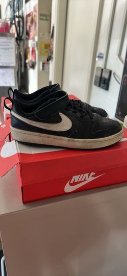 Used Nike Court Borough Low 2 (PSV) sneakers in size 2Y. These shoes are black with a white swoosh and white midsoles. The upper is made of leather an