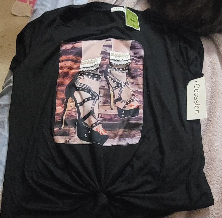 This black t-shirt with a high-heel graphic print is from the brand Occasion, as indicated by the tag attached to the shirt. It features a detailed im