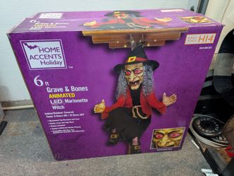 Home Accents Holiday Grave & Bones Animated Marionette Witch is a 6-foot tall hanging prop featuring a lit top structure, illuminated face, and moving