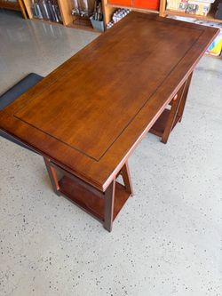 Brown wooden writing desk has a trestle-style base with two built-in shelves on each side.