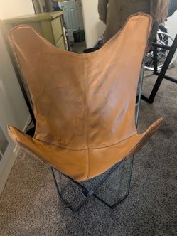 This is a vintage-style tan leather butterfly chair featuring a folding iron frame.