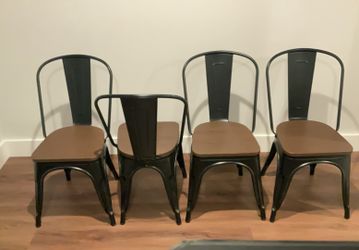 Four black metal dining chairs with faux wood seats
