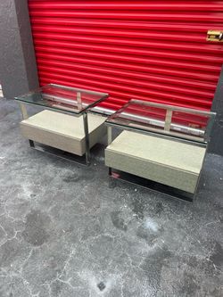 pair of modern bedside tables or nightstands featuring a chrome metal frame, glass top, and a built-in drawer