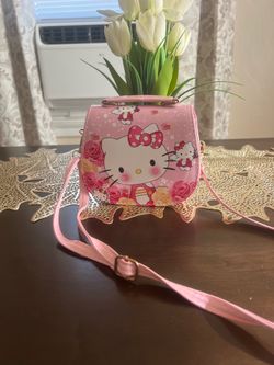 Cute pink Hello Kitty purse. Design has Hello Kitty with roses. Small handle on top. Adjustable shoulder strap. Gold-tone clasp and strap buckles.