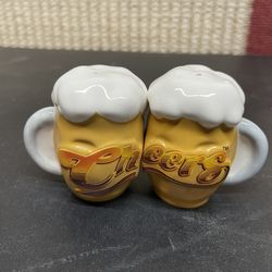set of vintage ceramic "Cheers" logo salt and pepper shakers shaped like beer mugs with frothy tops, often associated with TV memorabilia or bar kitsc