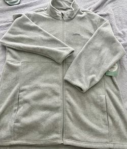 Soft light gray fleece jacket with a full front zipper. Features a stand collar and roomy hand pockets for warmth and convenience. Lightweight layer t