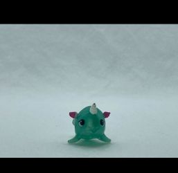 a Hatchimals CollEGGtibles Season 2 Snowflake Narwarbler mini figure by Spin Master. It is a small teal-green creature with a glittery pink tail-like