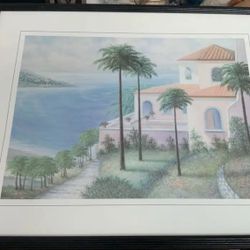 Framed print of a coastal scene with palm trees and a house. 