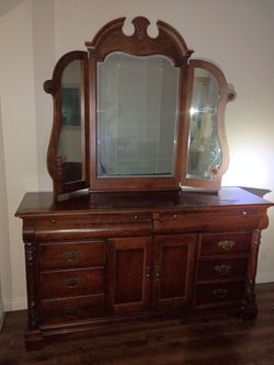 Universal Furniture triple dresser features a distinctive dark wood finish and includes a large, ornate tri-fold mirror.