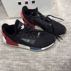 Adidas Men's NMD_R1 V2 sneakers in the "Core Black" colorway, featuring a black knit upper, Boost cushioning, and red and blue midsole plugs.
