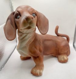 A vintage ceramic or porcelain Dachshund figurine that features an integrated mechanical music box mechanism
