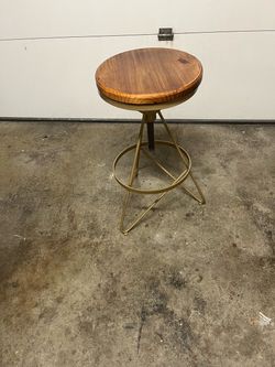 Industrial-style adjustable bar stool featuring a round wooden seat and a gold-toned metal base