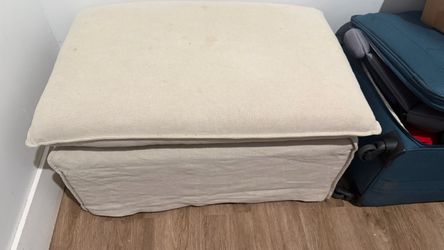 rectangular upholstered ottoman featuring a light beige fabric slipcover and a cushioned top