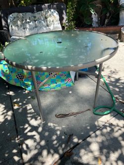 round outdoor table features a glass top and a beige metal frame.