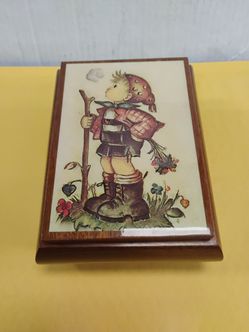 Vintage wooden music and trinket box featuring a decorative ceramic tile lid with an M.J. Hummel-style illustration.
Key Features