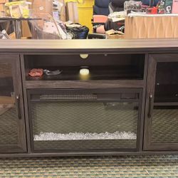 Beautiful dark wood TV stand with a built-in electric fireplace. This entertainment center offers plenty of storage while adding warmth and style to y