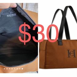 This is a brown canvas duffel bag with black faux leather handles and trim. It features a black embroidered monogram on the front and a zippered closu