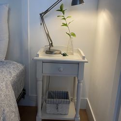 Pre-owned solid wood off white finish table with one drawer, scalloped edge on top and a lower shelf with a removable stripe lining basket.