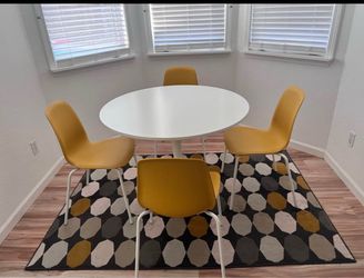 Round White Dining Table with 4 Yellow Chairs and rug.