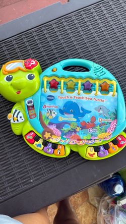 VTech Touch & Teach Sea Turtle, an interactive learning toy featuring a colorful sea creature book layout, light-up buttons, and piano keys.