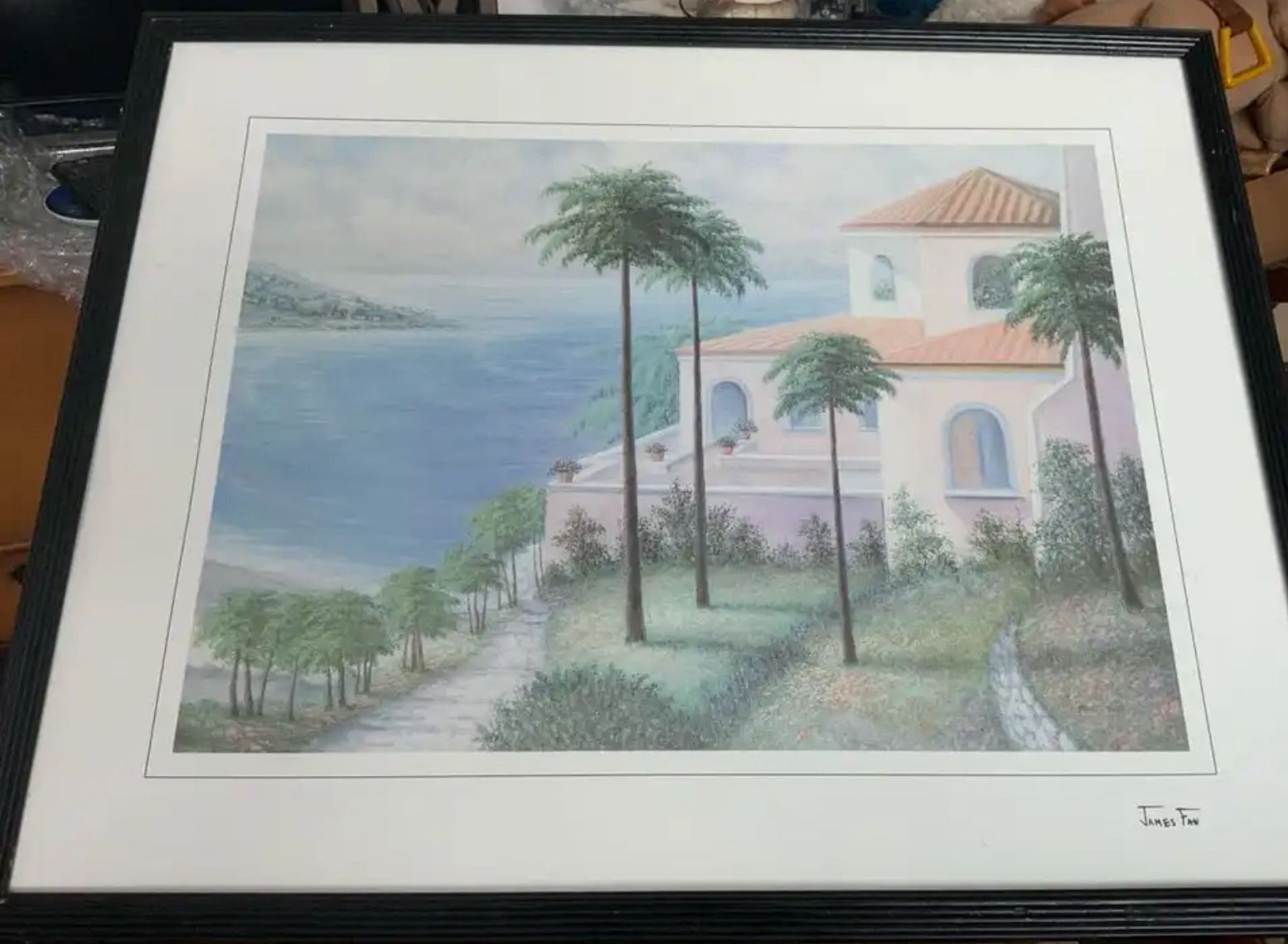 Framed print of a coastal scene with palm trees and a house.