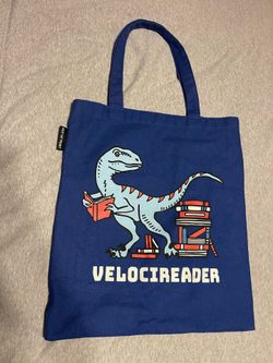 Velocireader tote - an Out of Print original design.  Product Details 100% cotton canvas Inner pocket Flat tote 15" w x 17" h 11" strap (hanging) Made