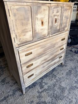 This vintage-style armoire features a whitewashed finish and distinct brass hardware pulls.