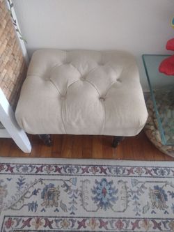 Foot stool cream-colored cushioned stool with dark, turned wooden legs.