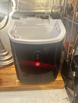 a portable countertop nugget ice maker with an interior white ice basket, scoop, and a glowing red power/clean button on the front control panel.