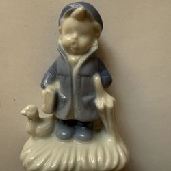 Vintage ceramic figurine depicting a young boy dressed in a raincoat and hat, holding an umbrella next to a small duck