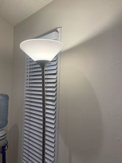 Modern floor lamp with a brushed silver metal pole and a white frosted plastic bowl shade. This lamp is powered by a standard cord and has a simple, m