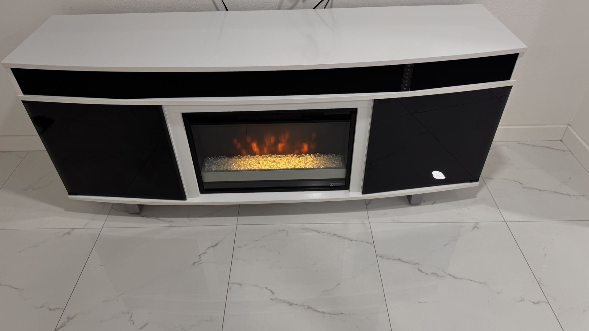 Consola moderna en blanco y negro con chimenea eléctrica integrada y sistema de sonido Bluetooth.