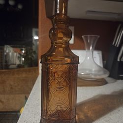 decorative Amber  glass bottle with a raised, ornate pattern and a cork stopper. 