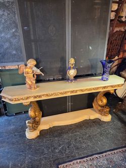 Carved and gilded wood console table in a classical style, featuring sculptural lower supports and ornamental relief details.