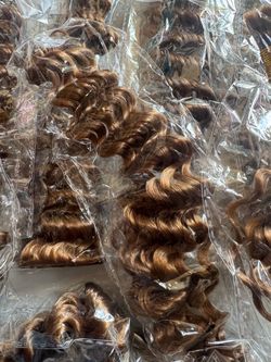 8 pack 27” bundles of deep wave synthetic hair extensions in #27 warm brown tone, each sealed in clear plastic packaging. Full, bouncy curl pattern th