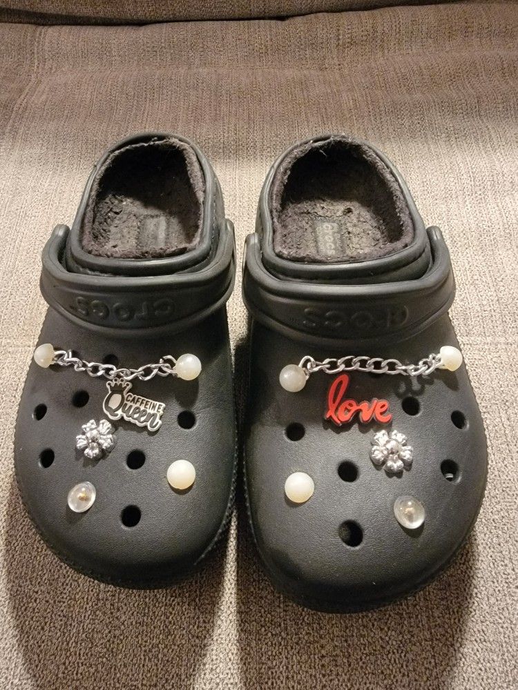 Black fur-lined Crocs clogs with Jibbitz shoe charms, pearl chains and decorative flower accents. Size 7