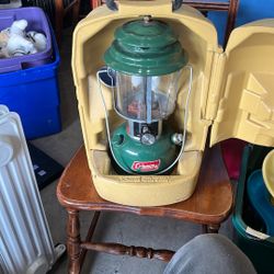 The image shows a vintage Coleman lantern, likely a Model 220 or 228 series, in a yellow plastic clamshell carrying case. These lanterns were produced