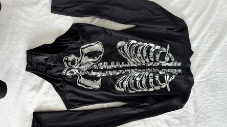 This is a black long-sleeve skeleton print bodysuit or one-piece swimsuit featuring a front zipper and white ribcage and pelvis graphics.