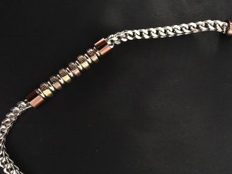 Collar para hombre de stainless steel. Tiene una combinación de cadenas con piezas cilíndricas en tonos cobre y dorado viejo.