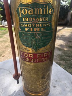 The image shows a vintage Foamite Crusader "Smothers Fire" brass fire extinguisher manufactured by the American-LaFrance Fire Engine Company i