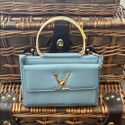 This black handbag is identified as the "Vivian Bag" by Shop Inez, featuring a "V" metal clasp and a gold top handle