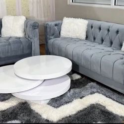 This living room features a two-piece set of furniture, including a sofa and a loveseat, both upholstered in gray velvet fabric. The pieces have a tuf